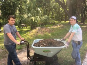 2 Wesley alumni helping do yard work with a wheelbarro